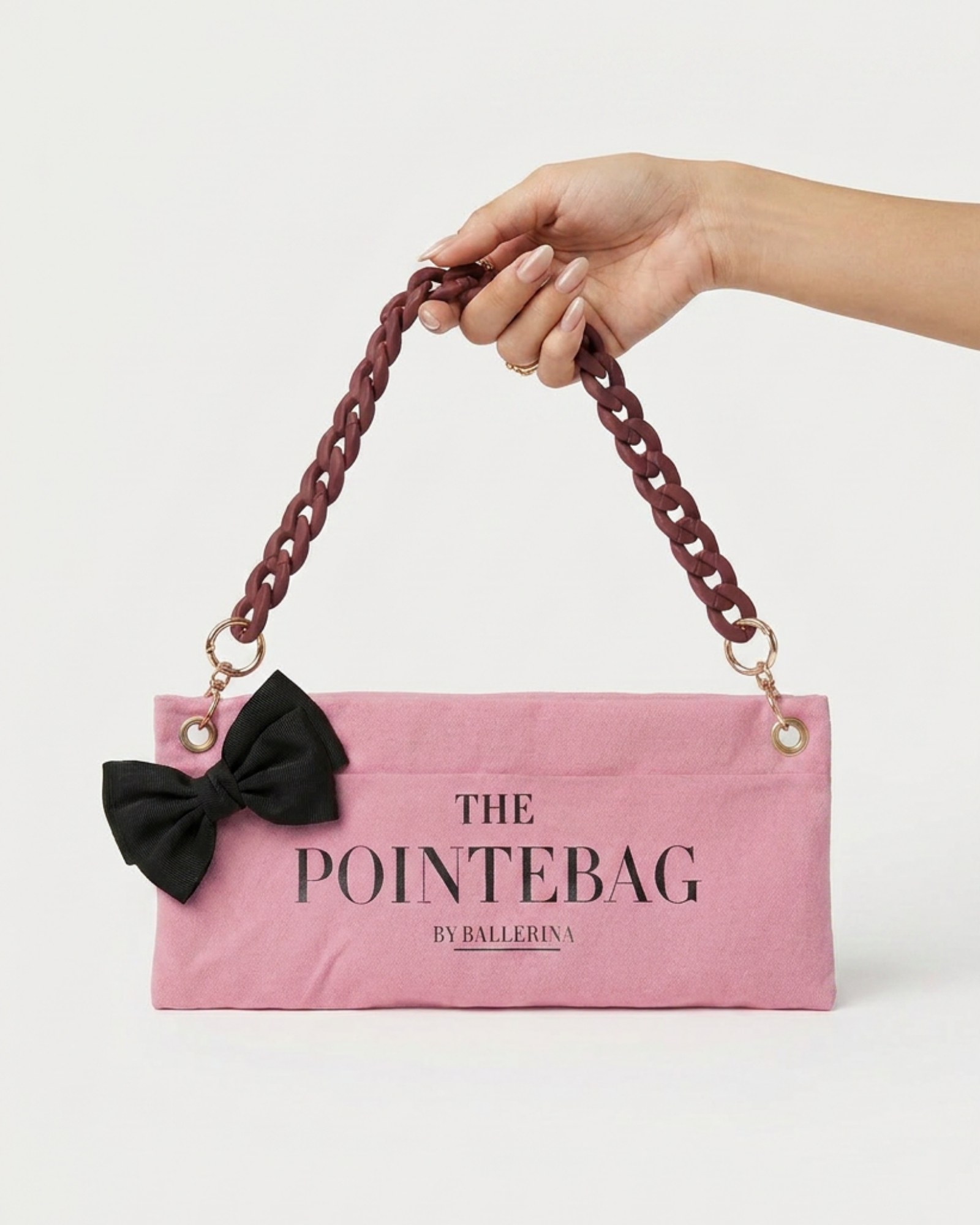 "Hand holding The PointeBag by Ballerina — pink ballet bag with black bow and burgundy chain strap"