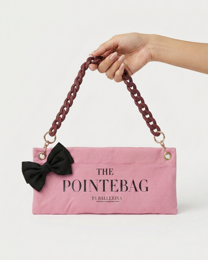 "Hand holding The PointeBag by Ballerina — pink ballet bag with black bow and burgundy chain strap"