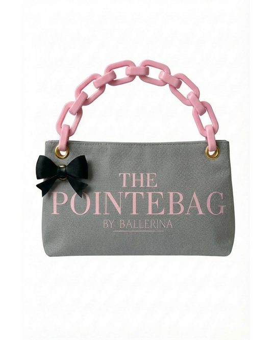 The front side of our Grey Classic PointeBag | The Logo PointeBag By ballerina is visibly seen taking the whole length of the bag. There are two gold eyelets on the top two corners where the pink plastic chain straps on. There is one more gold eyelet on the left side where a black bow clip snaps on.