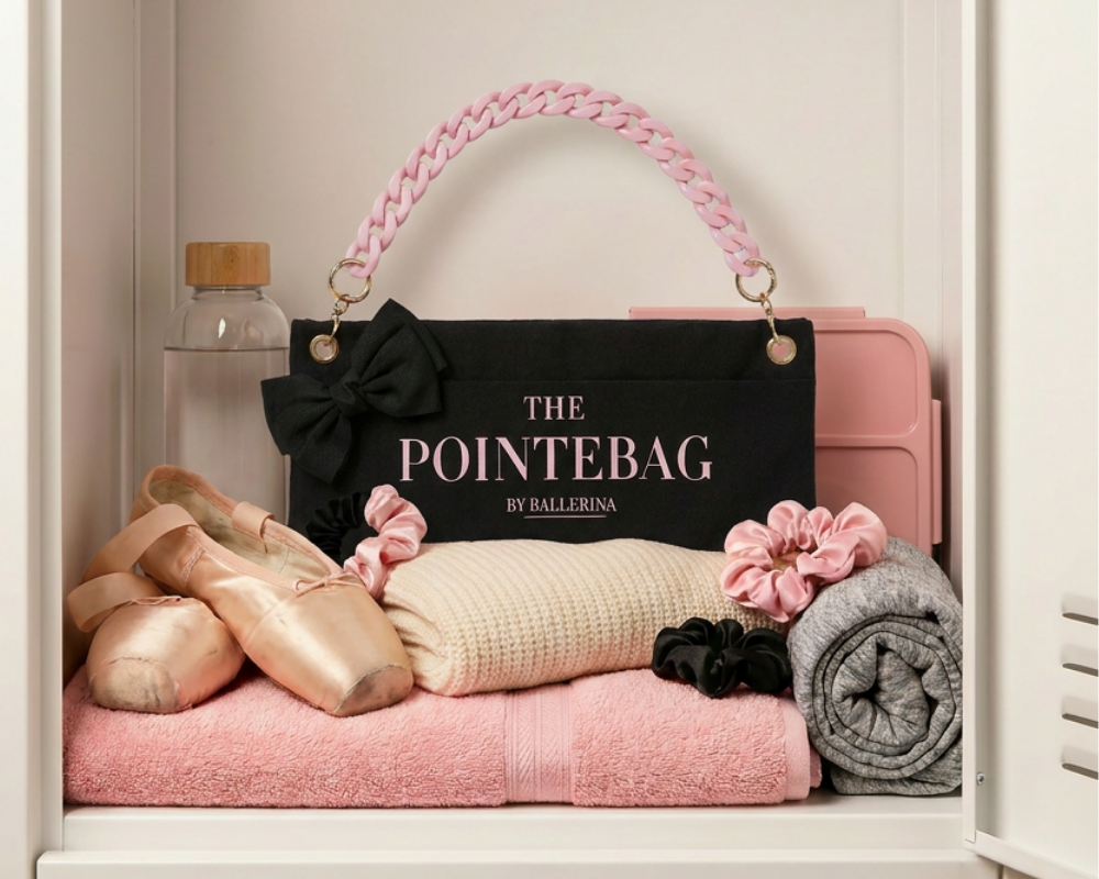 "The PointeBag By Ballerina in black with pink chain strap, styled in a ballet locker with pointe shoes, pink towel, and scrunchies"